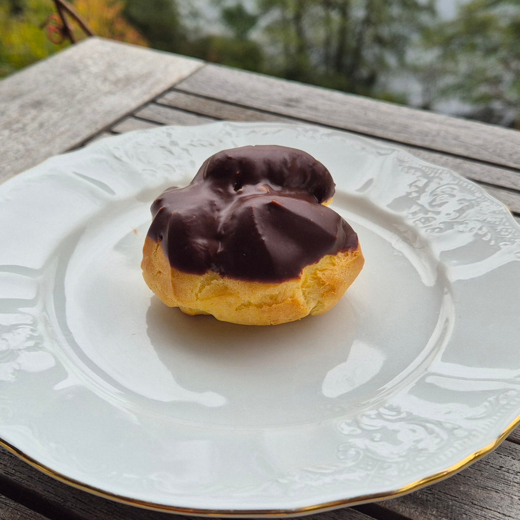 Chocolate-glazed pastry on a decorative plate with a blurred natural background